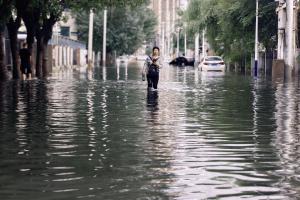 中国东北地区过去较少面对台风带来的持续性强降雨，今年也未能幸免。辽宁省会沈阳城区星期一（7月13日）多项雨量指标均创下1951年有完整气象记录以来最高纪录，传统的“南涝北旱”格局被打破。图为沈阳一名女子7月14日走在淹水的街上。（法新社）