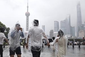 受台风“白海豚”影响，上海星期天（8月9日）普降大雨，上海市气象台当天10时30分更新中心城区暴雨橙色预警信号为暴雨红色预警信号。图为游客冒雨行走在外滩街头。（中新社）
